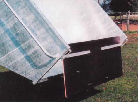 Feuerverzinkter Kuli gekippt, mit leicht geöffneter, brauner Frontklappe aus Holz, steht auf Gras, seitliche Ansicht des Grossraumkulis, Klappe zentral