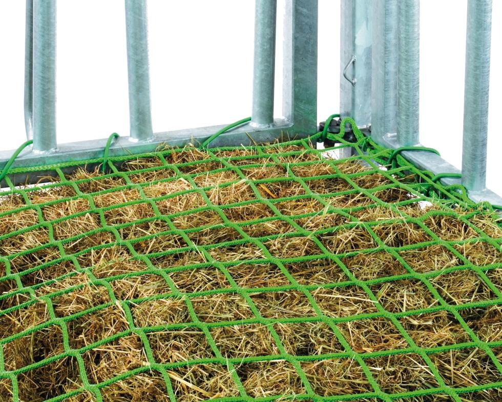 Eine Detailansicht aus einer Ecke einer Raufe, grünes Futtersparnetz, befestigt an Raufe, teilweise sind Rundbogengitter zu sehen, unter dem Netz ist Futter zu sehen