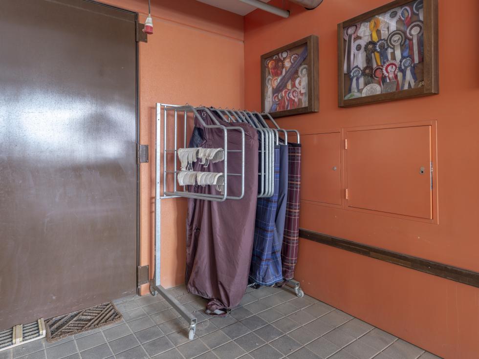 Ein Deckenhalter auf fahrbarem Gestell mit zehn Aufhängungen gefüllt mit diversen Decken, stehend in einer Ecke vor oranger Wand