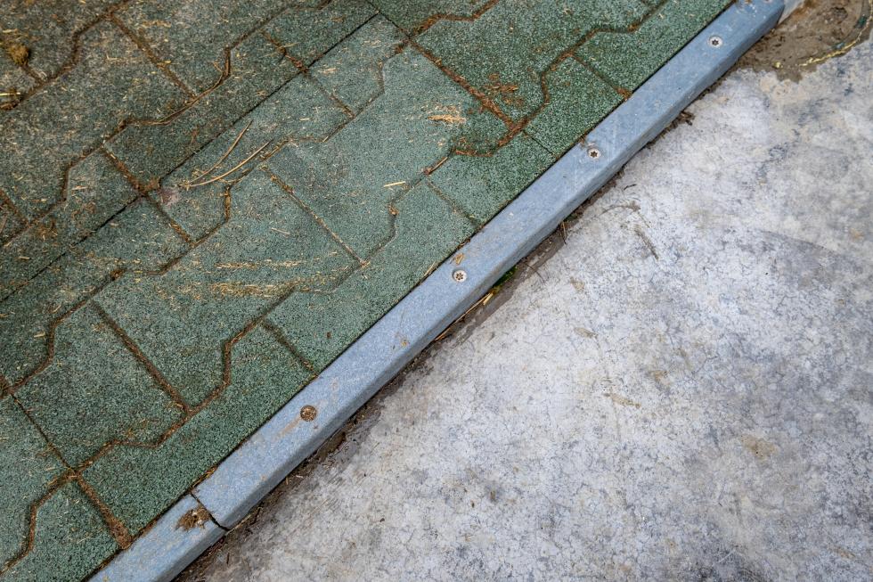 Eine Anschlagsleiste, vierkant, aus grauem Recyclingkunststoff mit Edelstahlschrauben fixiert, Zwei Komfortexplatten aus Elastikpflastersteinen an Leiste angeschlagen, blaue Verbindungszäpfchen auf rechter Seite sichtbar, Draufsicht 