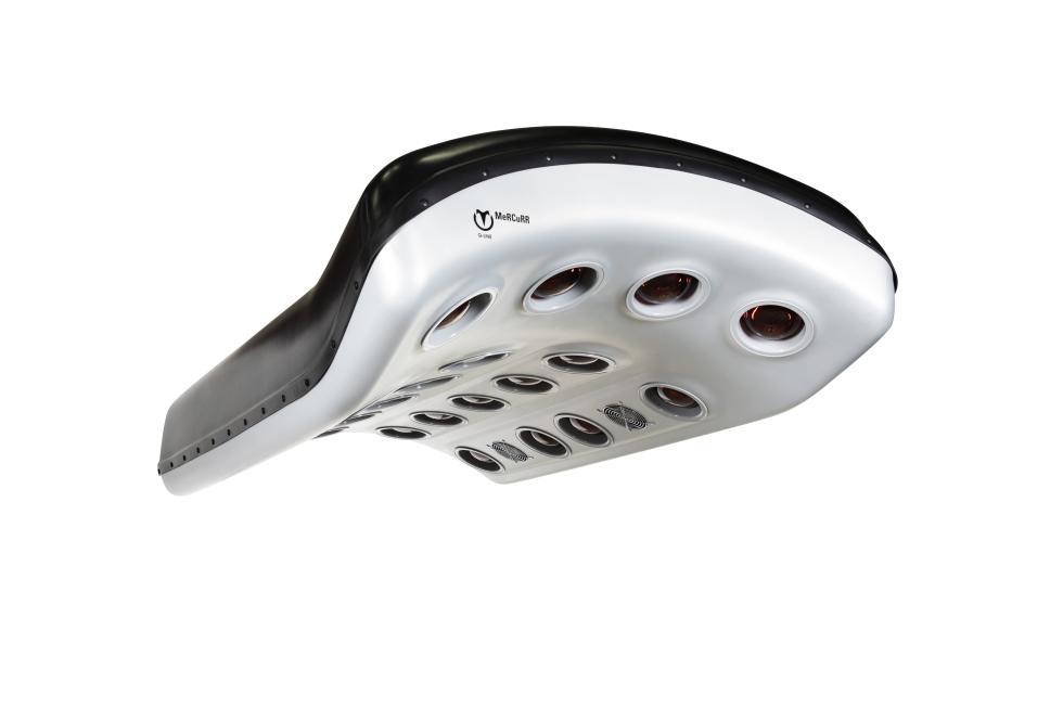 Ein Pferdesolarium, zweifarbig, grüner und grauer Kunststoff, leicht gewölbt und gebogen, mit roten und andersfarbigen Lampen, sowie Ventilatoren auf der Unterseite, aufgehängt in Stallgang, roter Boden, rechts und links Pferdeboxen, auf jeder Seite schaut jeweils ein schwarzes Pferd in den Gang hinaus