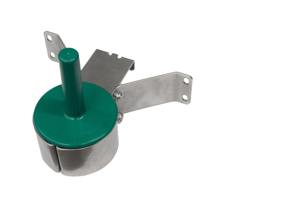 In metallischer, dreibeiniger Lecksteinhalter, eingesteckt und montiert an Flacheisen, am Ende der drei Beine befindet sich eine Rundung im Flacheisen, auf welcher ein grüner Kunststoffstab auf einer Platte befestigt ist, verschraubt an Holzwand, eine Person hängt den dreibeinigen Halter aus der Montageplatte aus